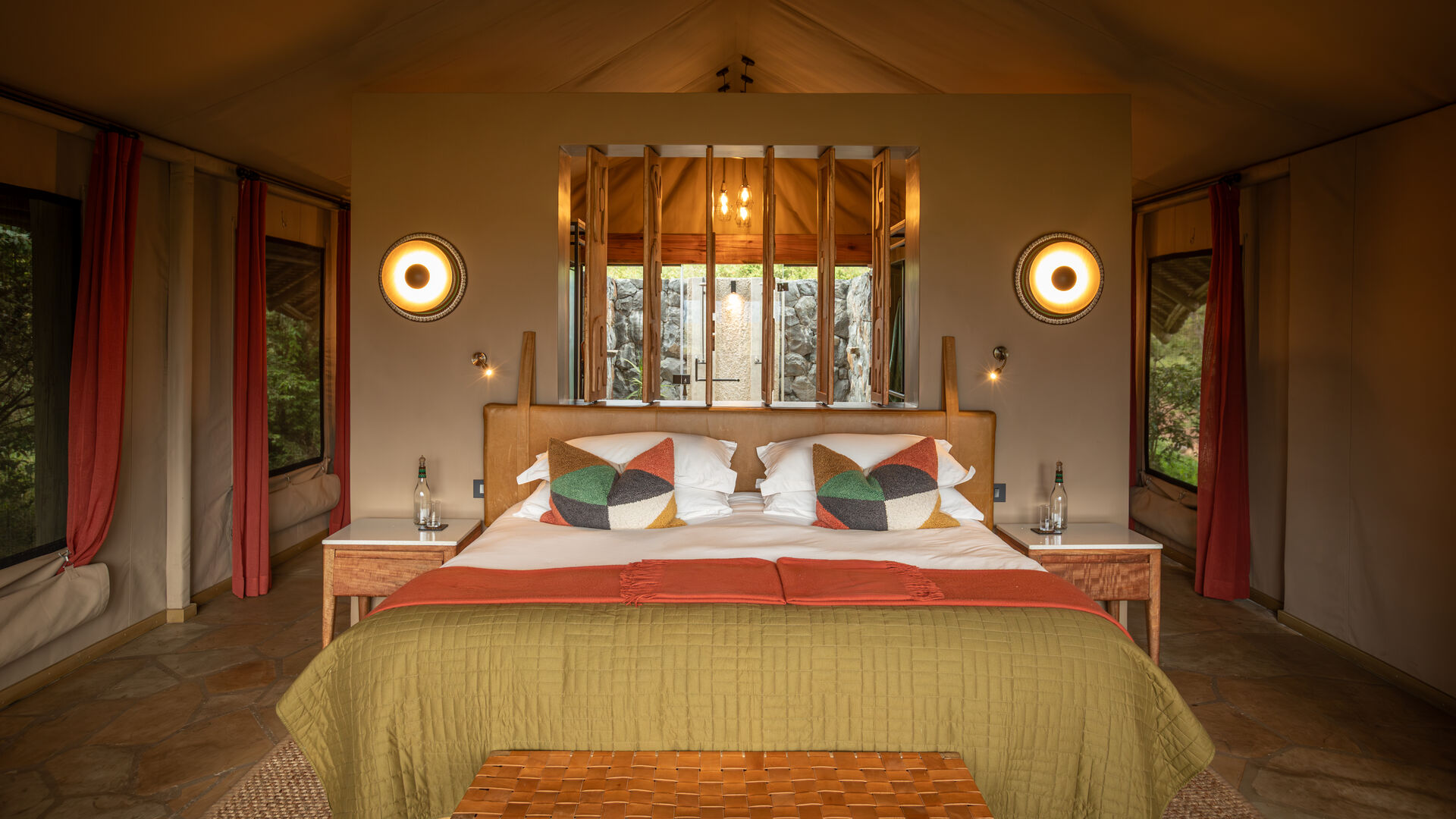 A bedroom at Naboisho Camp with a large bed, patterned cushions, and soft lighting on either side