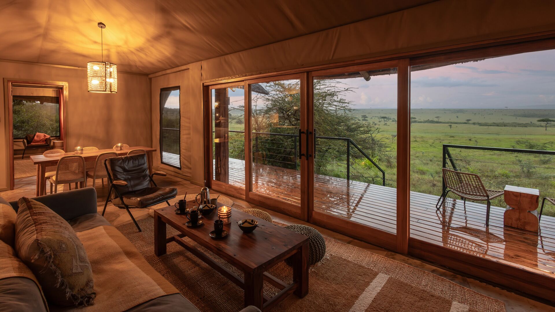 The family suite interior of Naboisho's luxury safari family suite with lounge and dining area, sliding glass doors, and a wooden deck overlooking expansive savannah views.