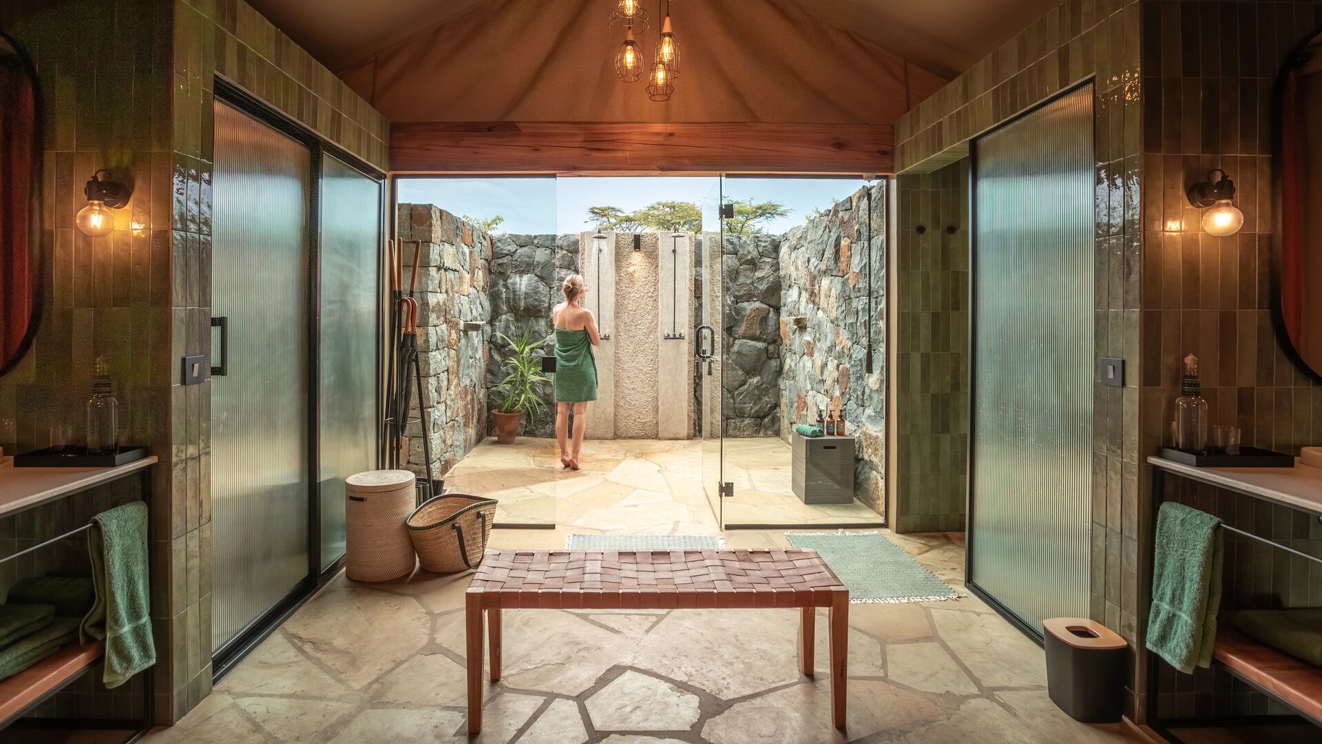 Naboisho's pen-air safari bathroom with stone walls, twin indoor wash areas, and a private outdoor shower courtyard.