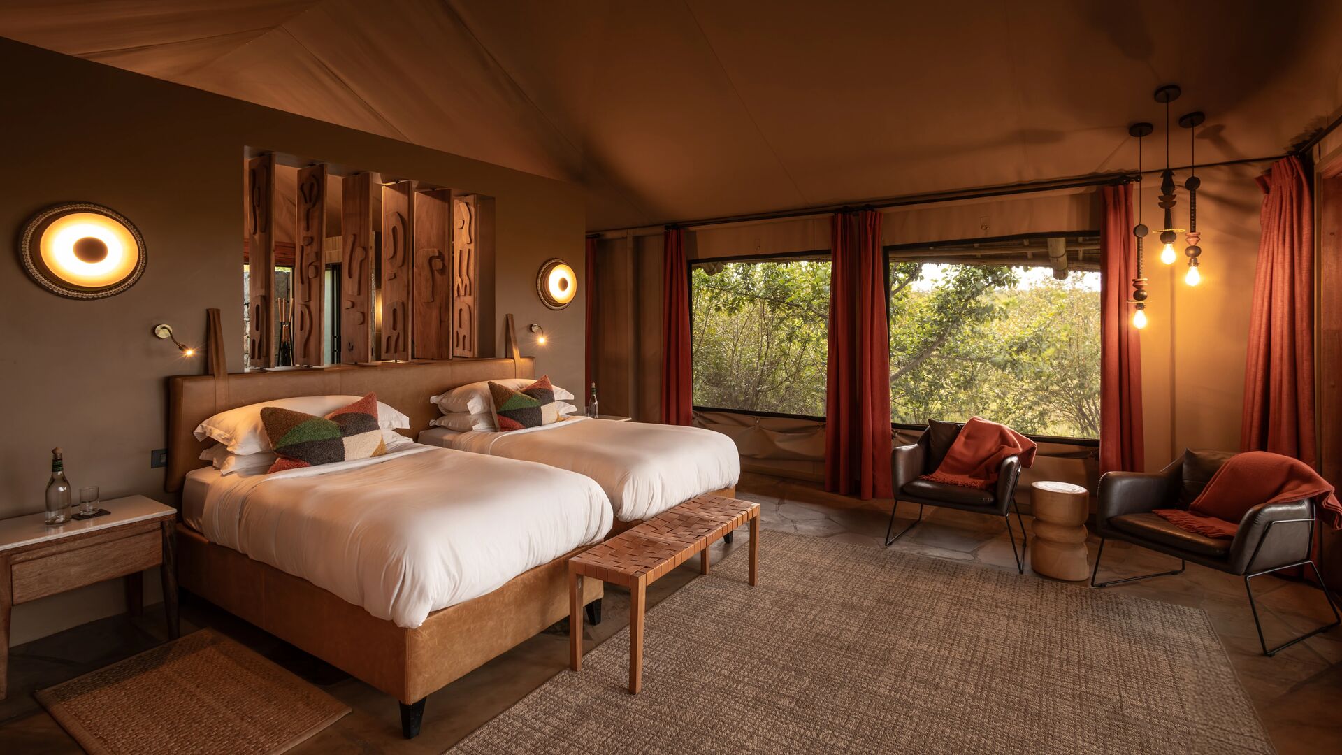 Interior of a luxury twin at Naboisho camp room featuring two beds, warm lighting, woven textures, and large windows overlooking surrounding conservancy.