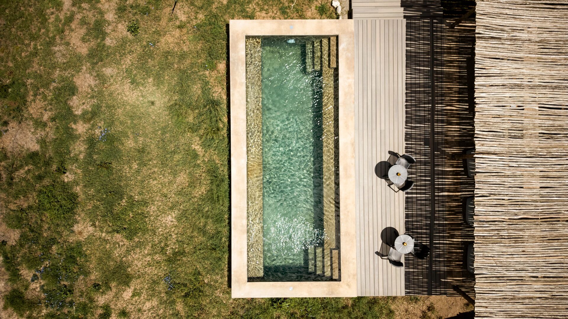 Overhead view of a private plunge pool at Namiri Retreats beside a wooden deck with chairs, set within grassy savannah and shaded by natural textures.