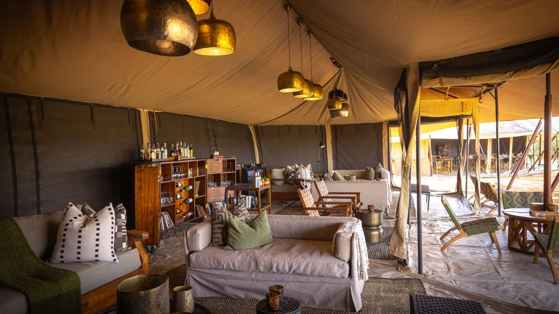 The interior of Olakira's lounge with comfortable seating, wooden bar shelves, hanging lantern lights, and open canvas walls leading to outdoor dining areas.