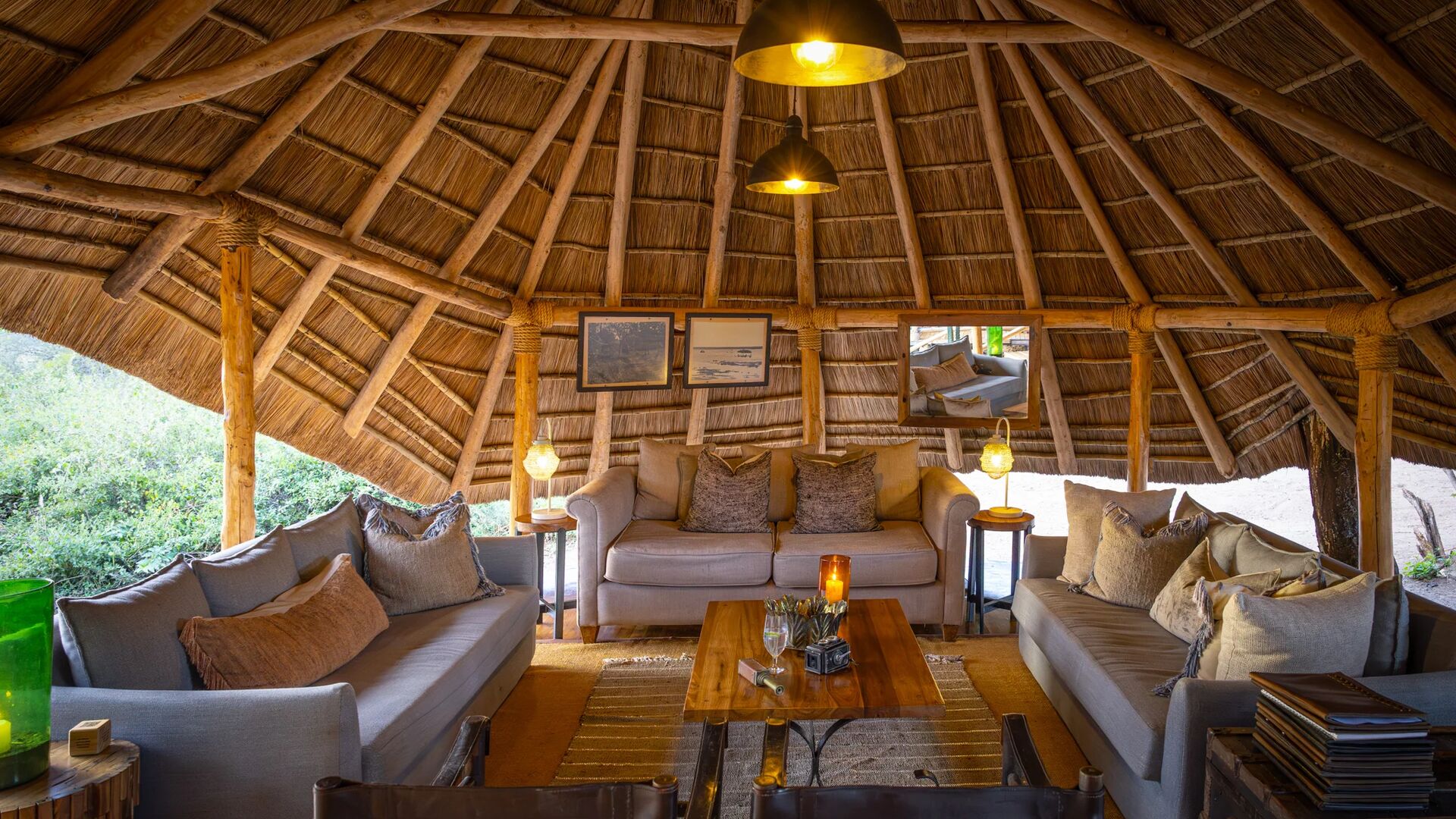 The interior of the circular thatched safari lounge at Oliver's Camp with comfortable sofas, soft lighting, wooden furniture, and a relaxed seating area designed for guests to unwind.