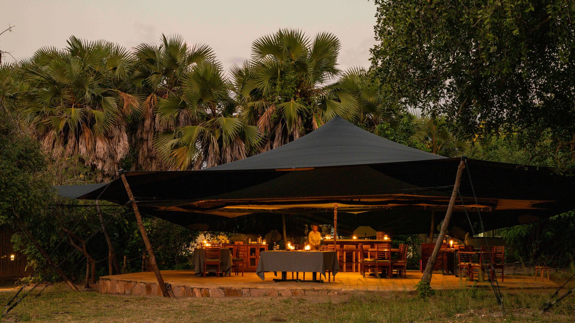 Roho ya Selous' open-air dining area under a canopy warmly lit with candles at dusk