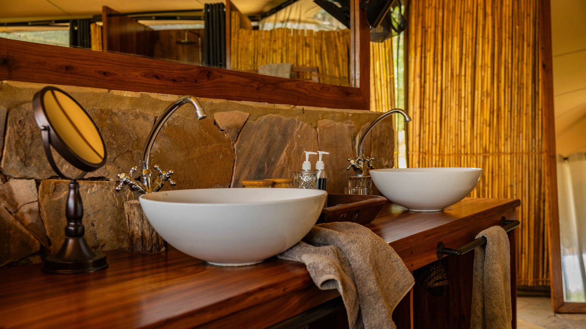 A guest bathroom at Roho ya Selous with double sinks, wooden counter, and bamboo walls