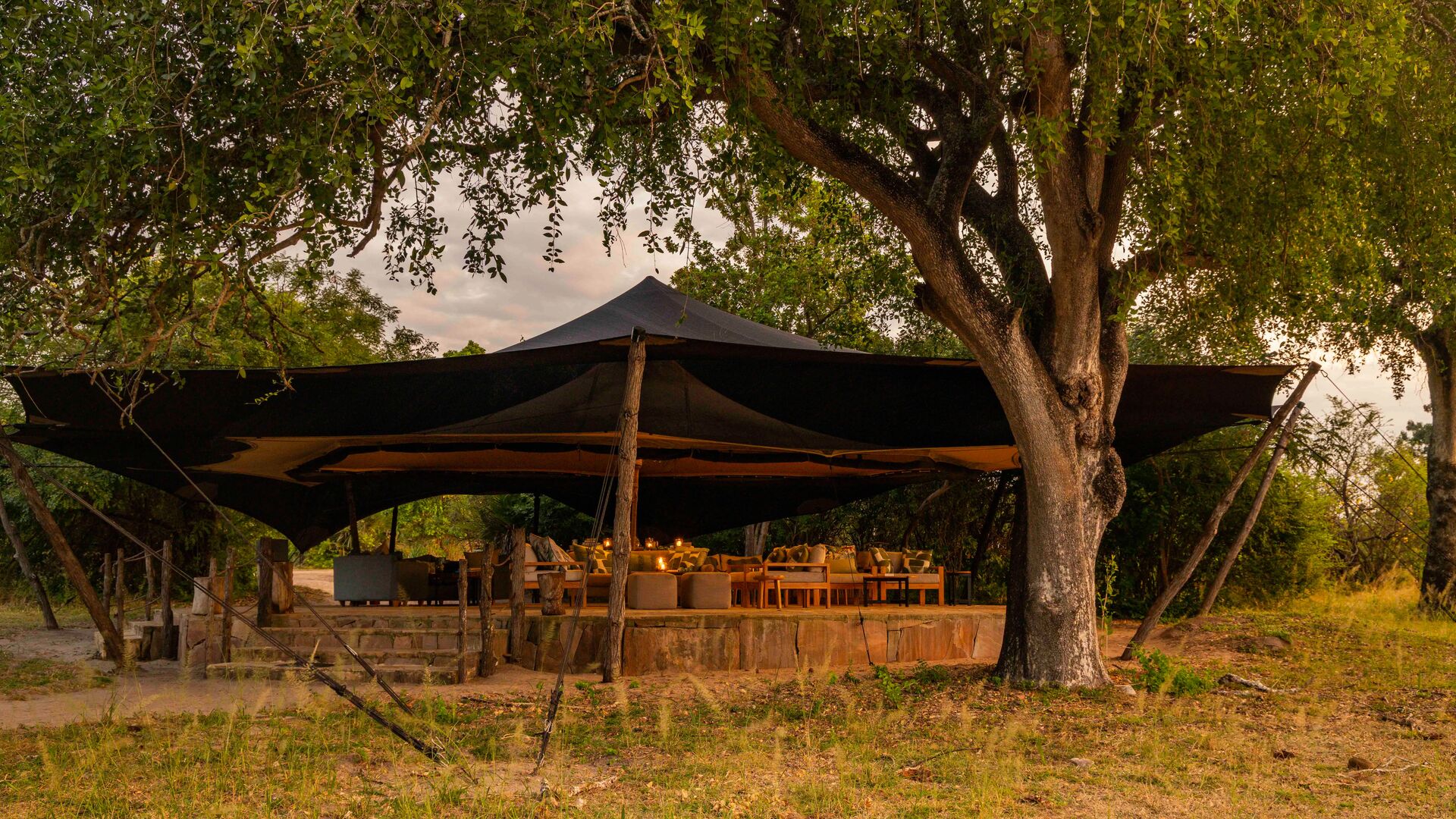 Roho ya Selous' lounge and dining area surrounded by trees and softly lit in the evening