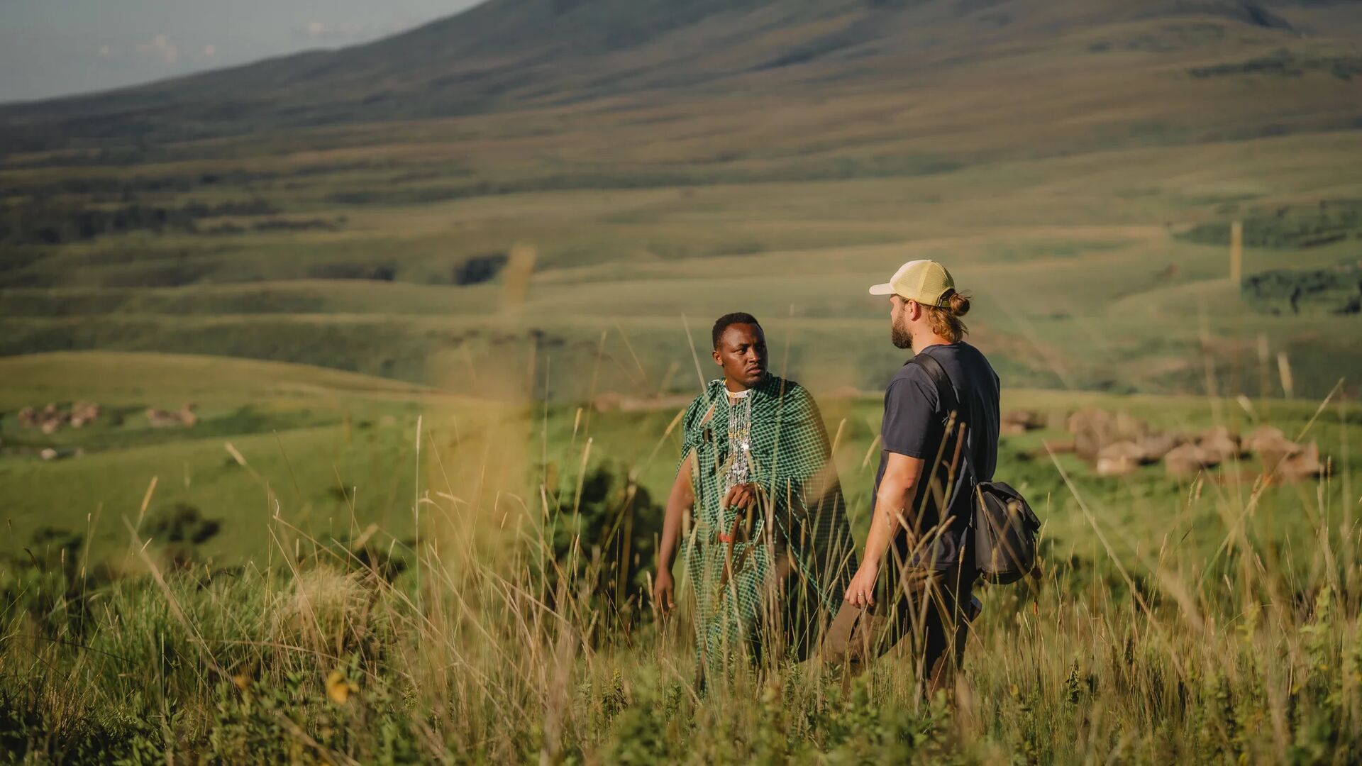 A guide and guest standing in tall grass discussing the landscape with rolling hills in the background