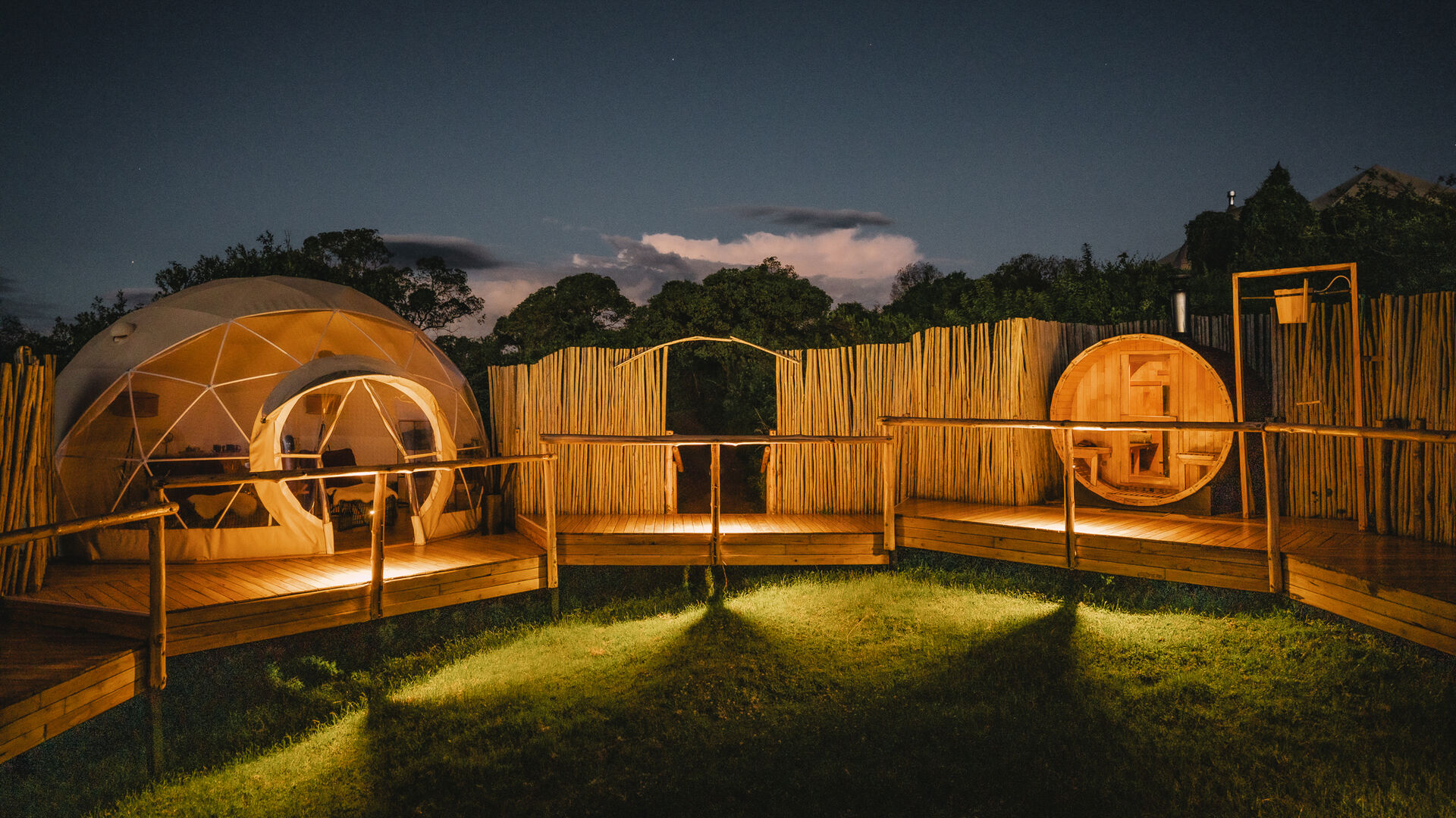 A lit spa area with dome structures and wooden decks surrounded by fencing at night