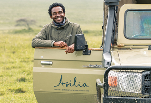 Male Asilia staff member smiling and leaning on the safari vehicle door