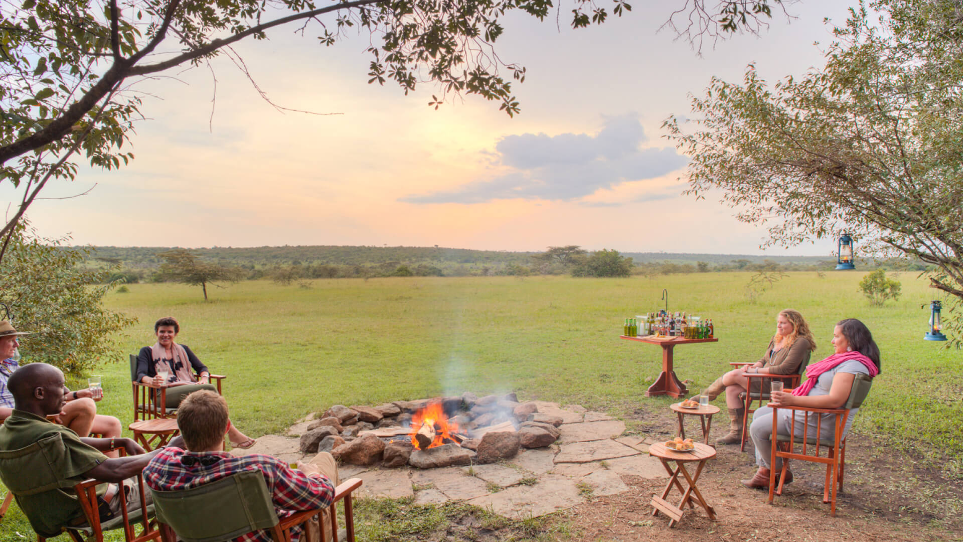 Guests around the campfire enjoying sundowners at sunset, mara naboisho conservancy, kenya, encounter mara camp