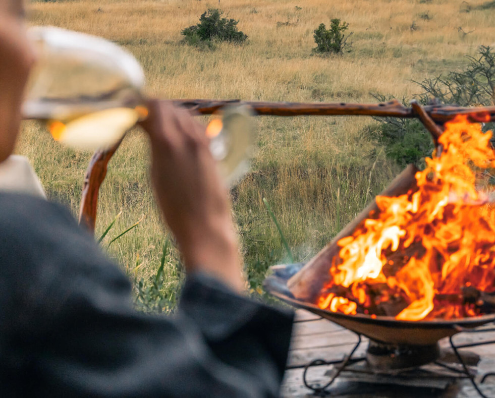 guest enjoying wine by the campfire, mara naboisho conservancy, kenya, encounter mara camp