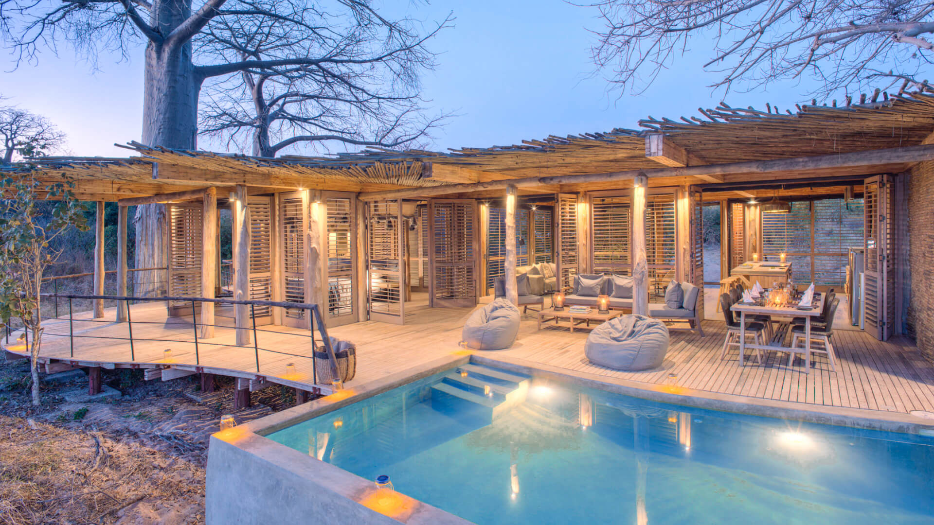 Jabali Private House, Ruaha National Park, house lit up with lanterns once the sun has set, blue pool, tables, chairs, loungers and bean bags for seating, shutter doors open