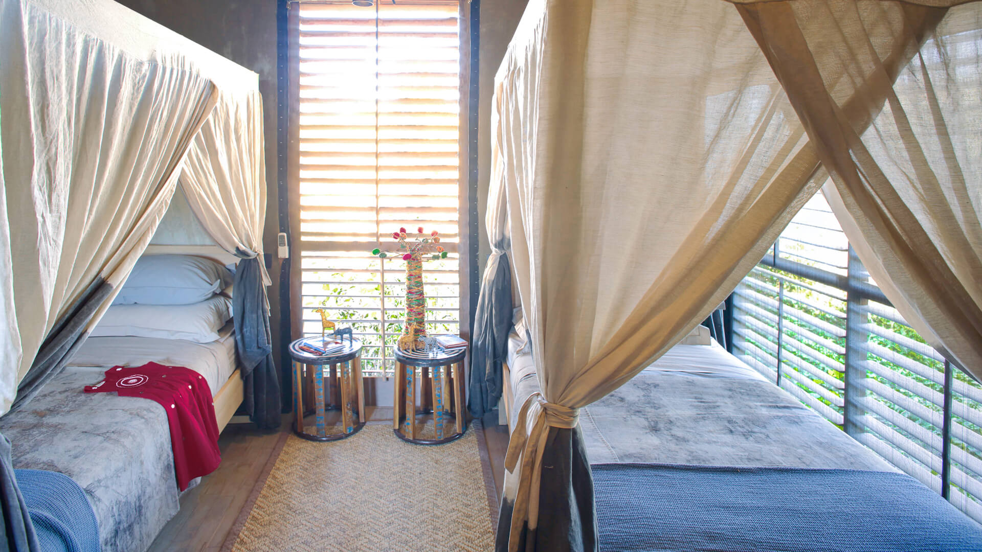 Jabali Private House, Ruaha National Park, twin beds with bedside tables with ornaments and mosquito nets hanging from the beds, rug between the beds