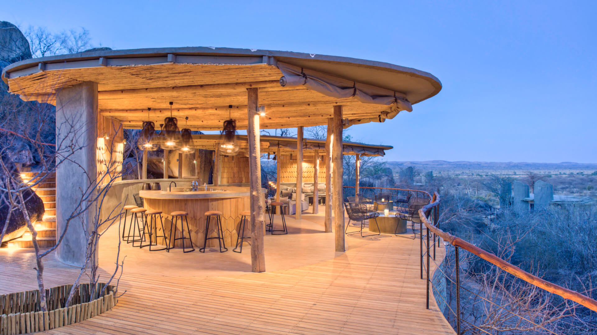 Jabali Ridge, Ruaha National Park, deck with a view of the park, bar stools and hanging lights with chairs and tables on the deck