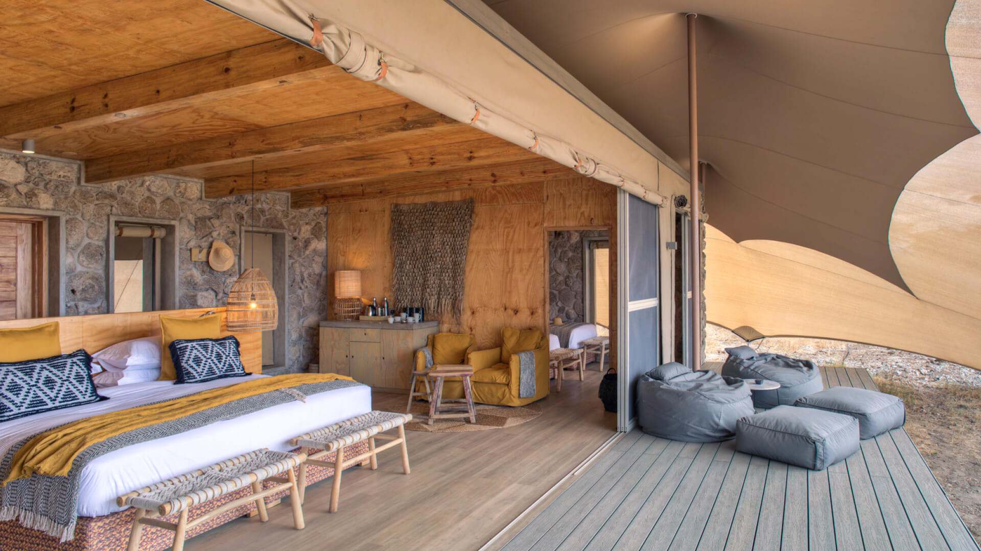 Namiri Plains, Serengeti National Park, view of the interior, double guest tent, bed with pillows and throw blanket, hanging lights, lamp on the side table with coffee station, bean bags on the deck, doors open