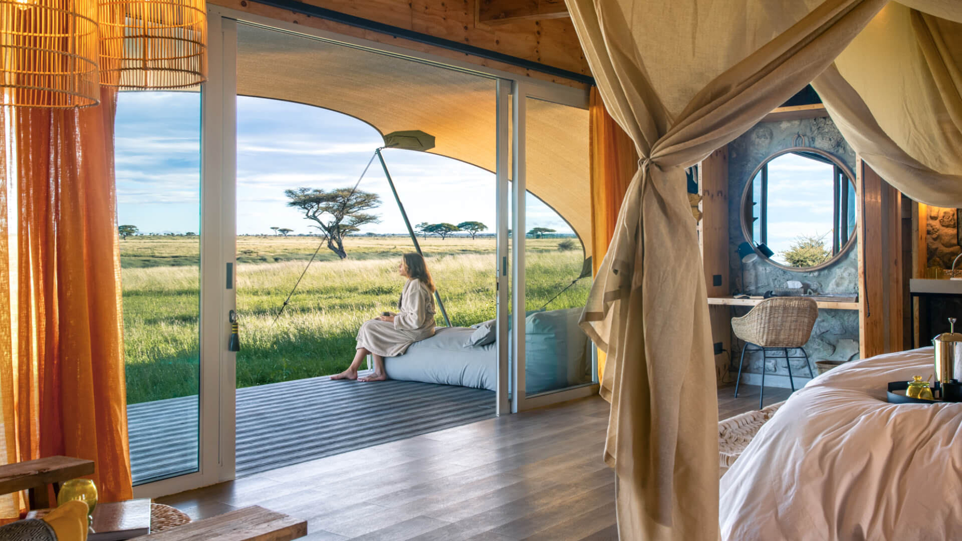 Namiri Plains Retreat, Serengeti National Park, guest sitting on the deck with a cup of coffee outside the room, door open