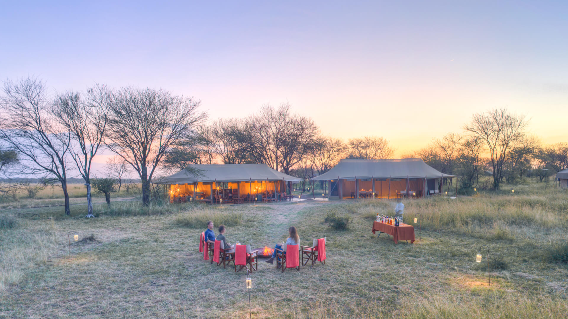 Guests enjoying sundowners around the campfire at camp, olakira migration camp, Serengeti National Park, Tanzania
