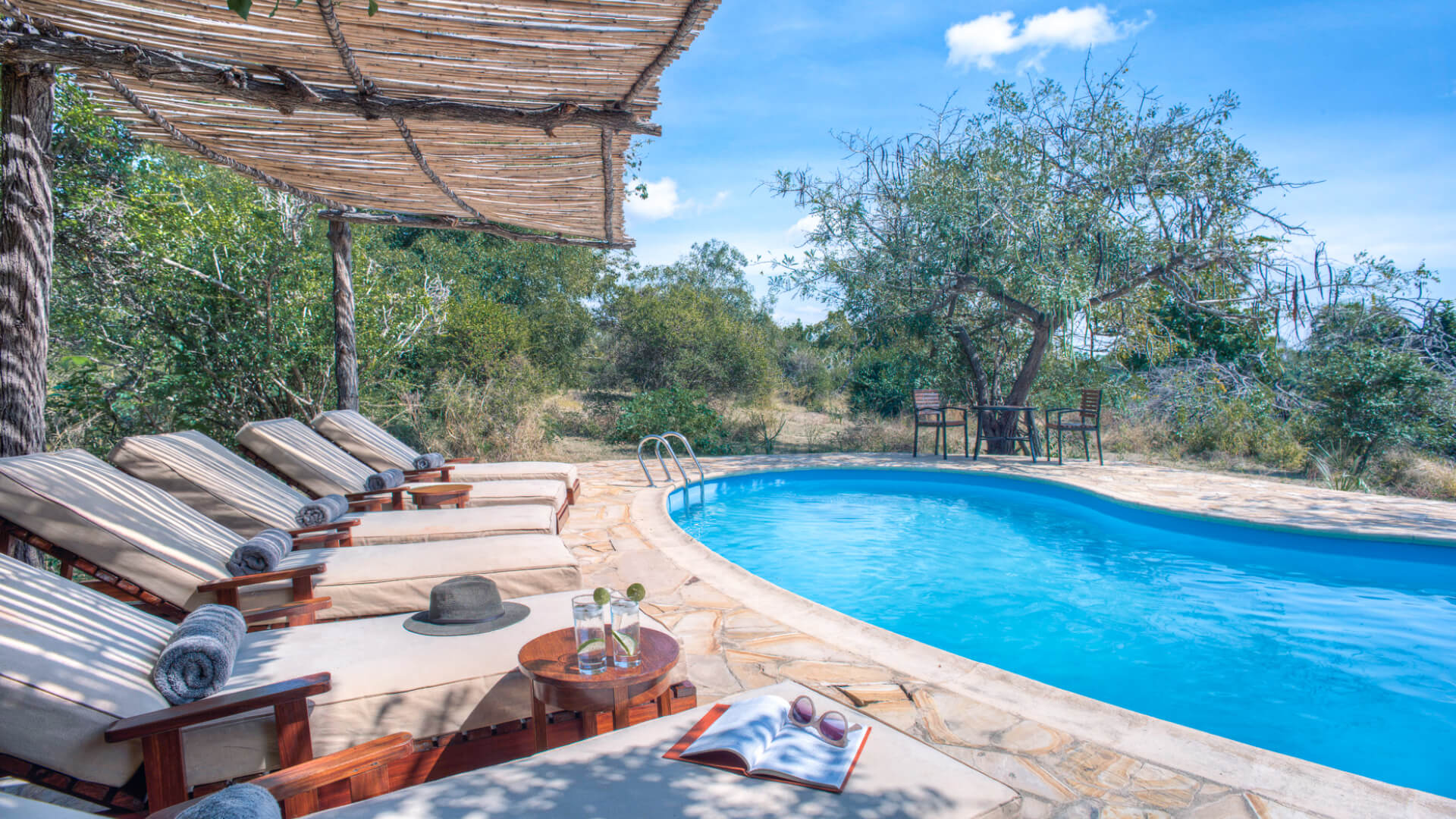 Roho ya Selous Camp, Nyerere National Park, loungers by the pool area, drinks on table, book and sunglasses and hat