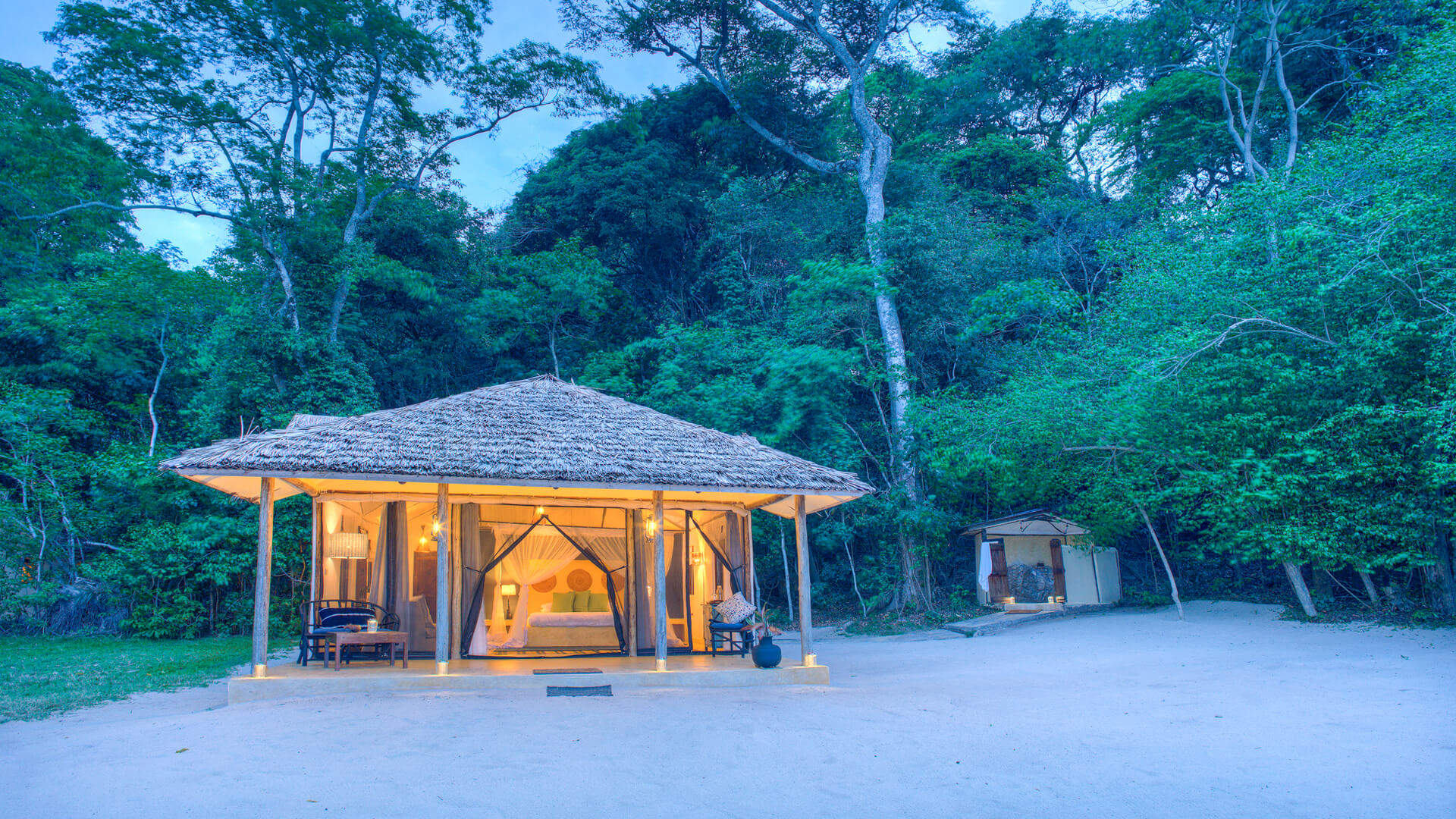 Rubondo Island Camp, Lake Victoria, exterior view of the chalet amongst the lush green trees lit up after dusk