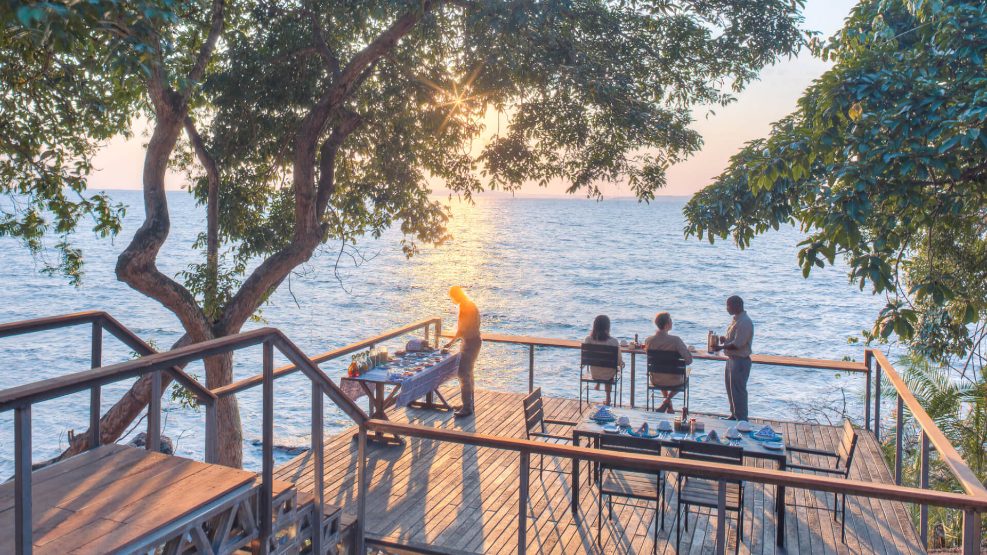 Rubondo Island Camp, guests being served coffee while they watch the sunrise, camp staff preparing breakfast setup