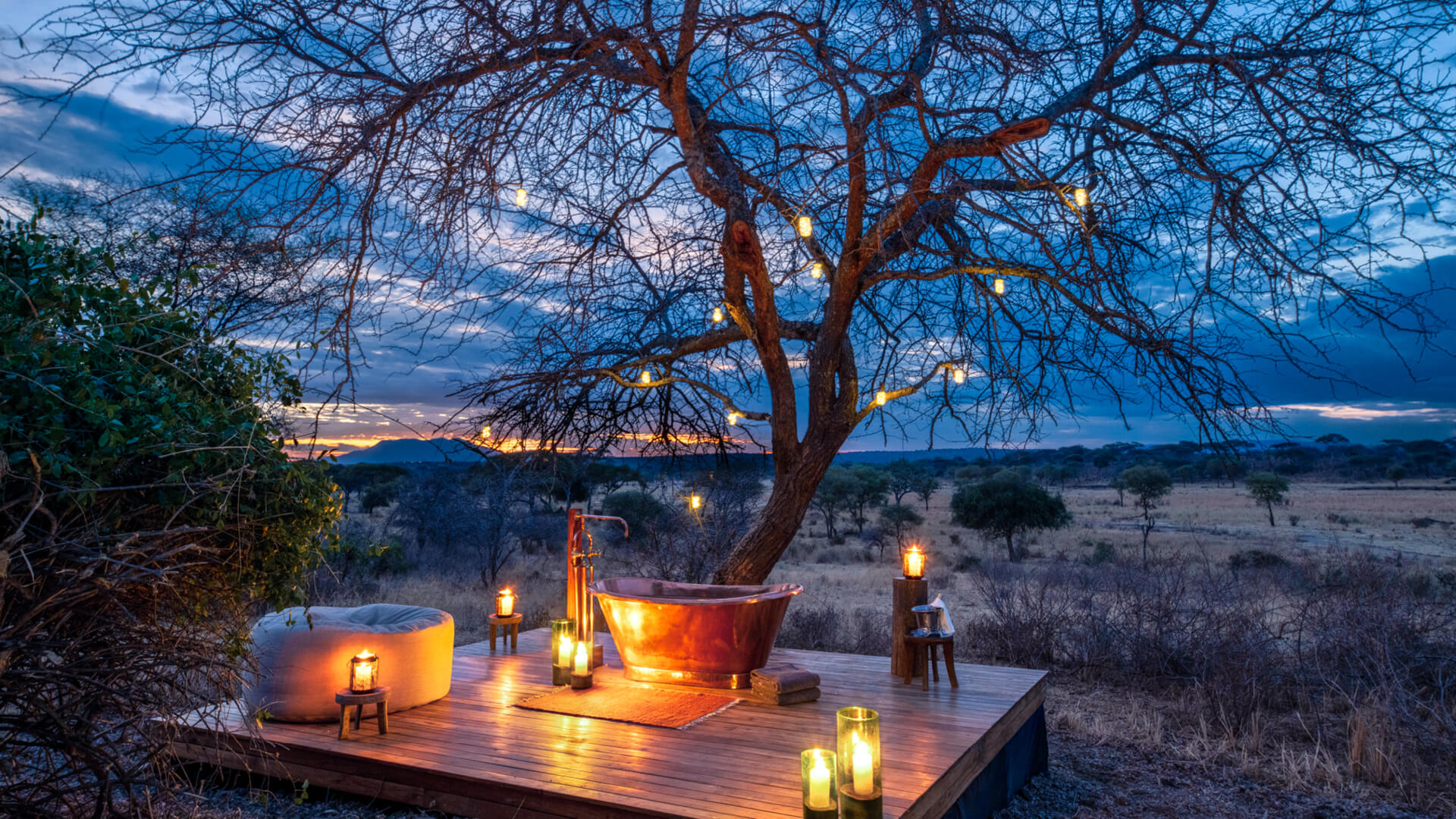 A romantic bath set up - a copper tub on a wooden deck surrounded by candles.
