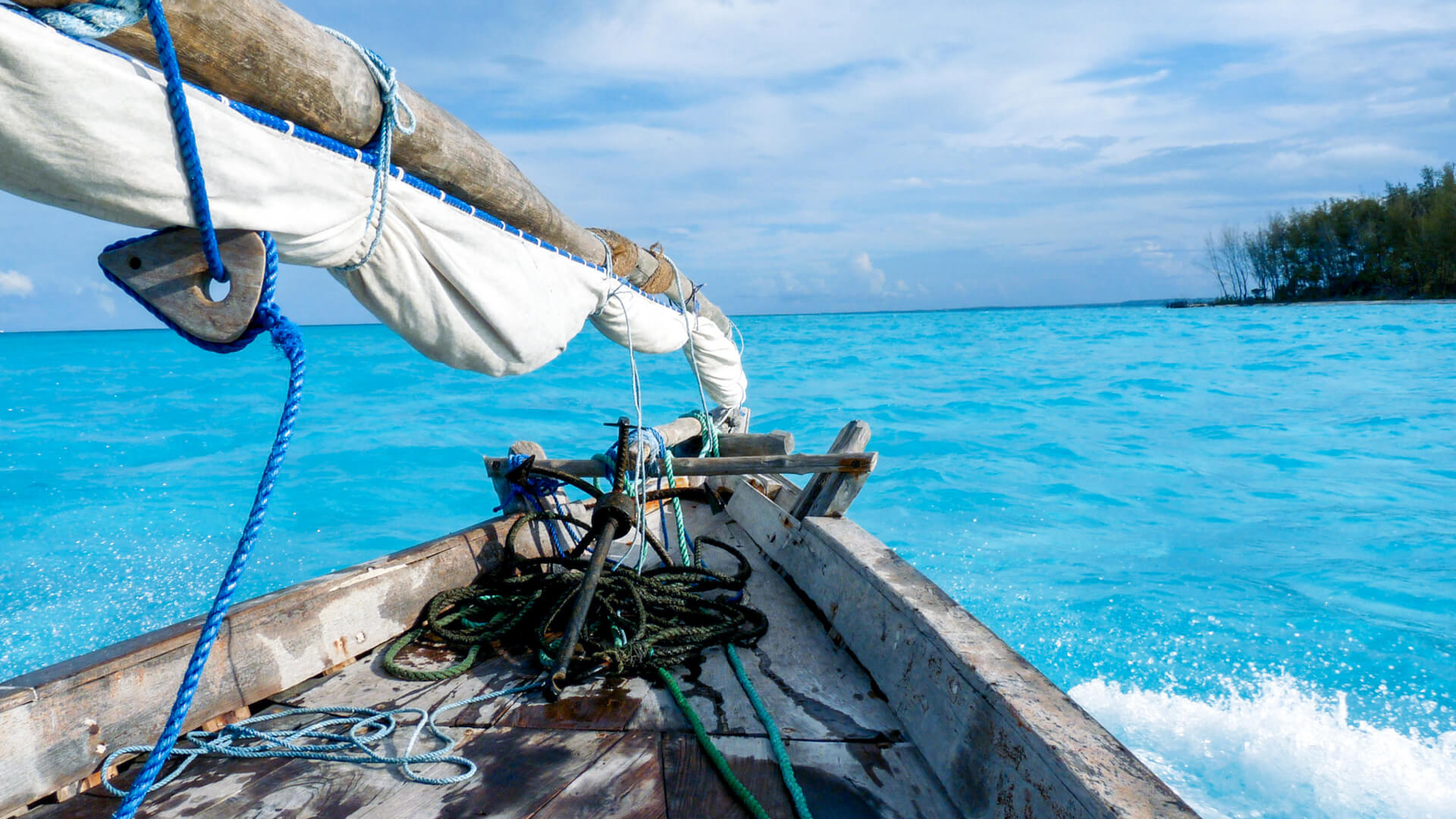 A traditional sailing dhow splashes through the turquoise waters of Zanzibar