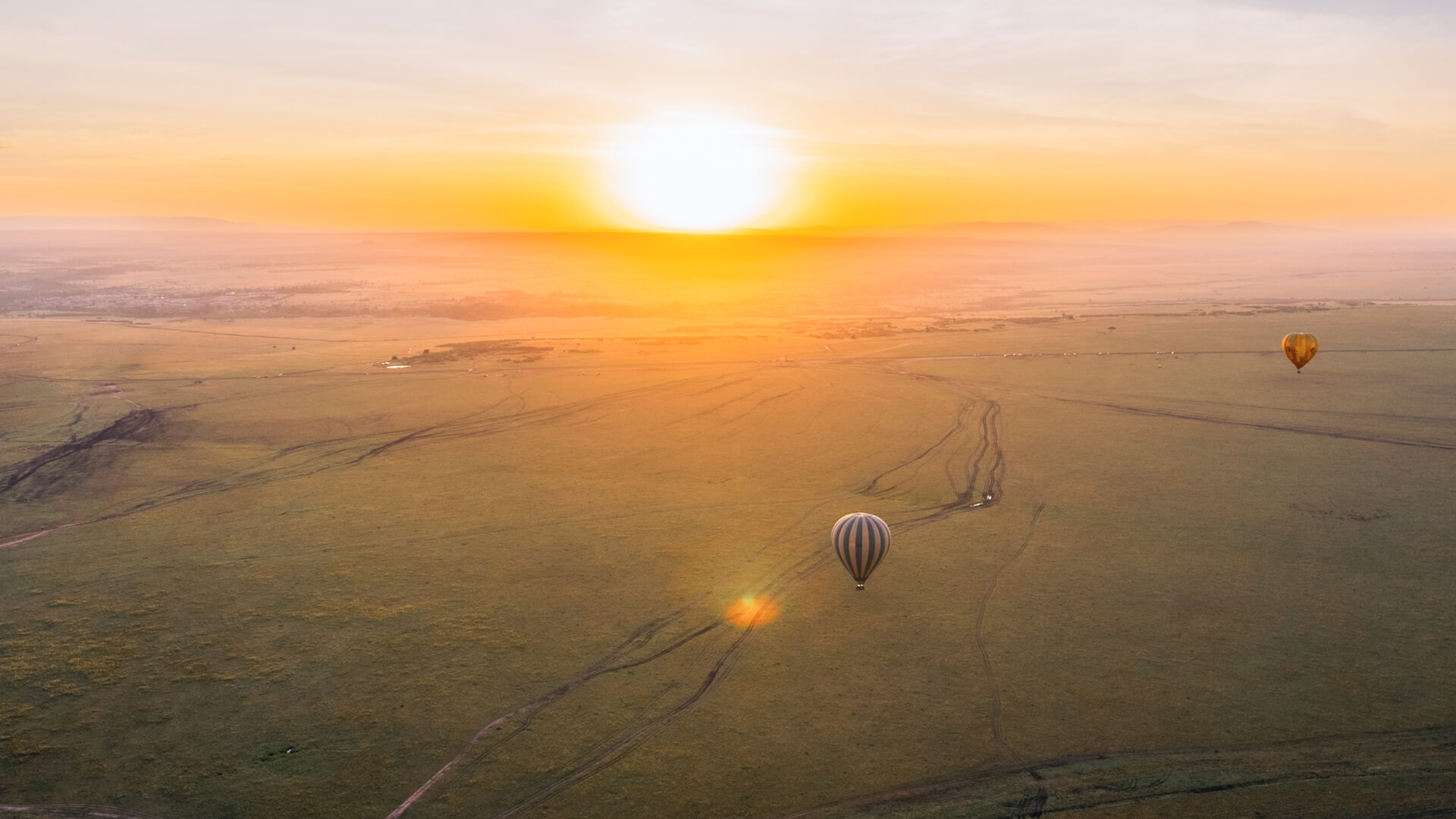 A hot air balloon glides over the plains at sunrise