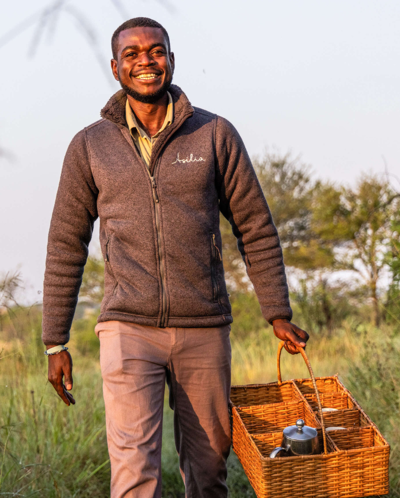 male asilia staff smiling at the camera, delivering morning coffe to guests, olakira camp, serengeti, tanzania, asilia africa