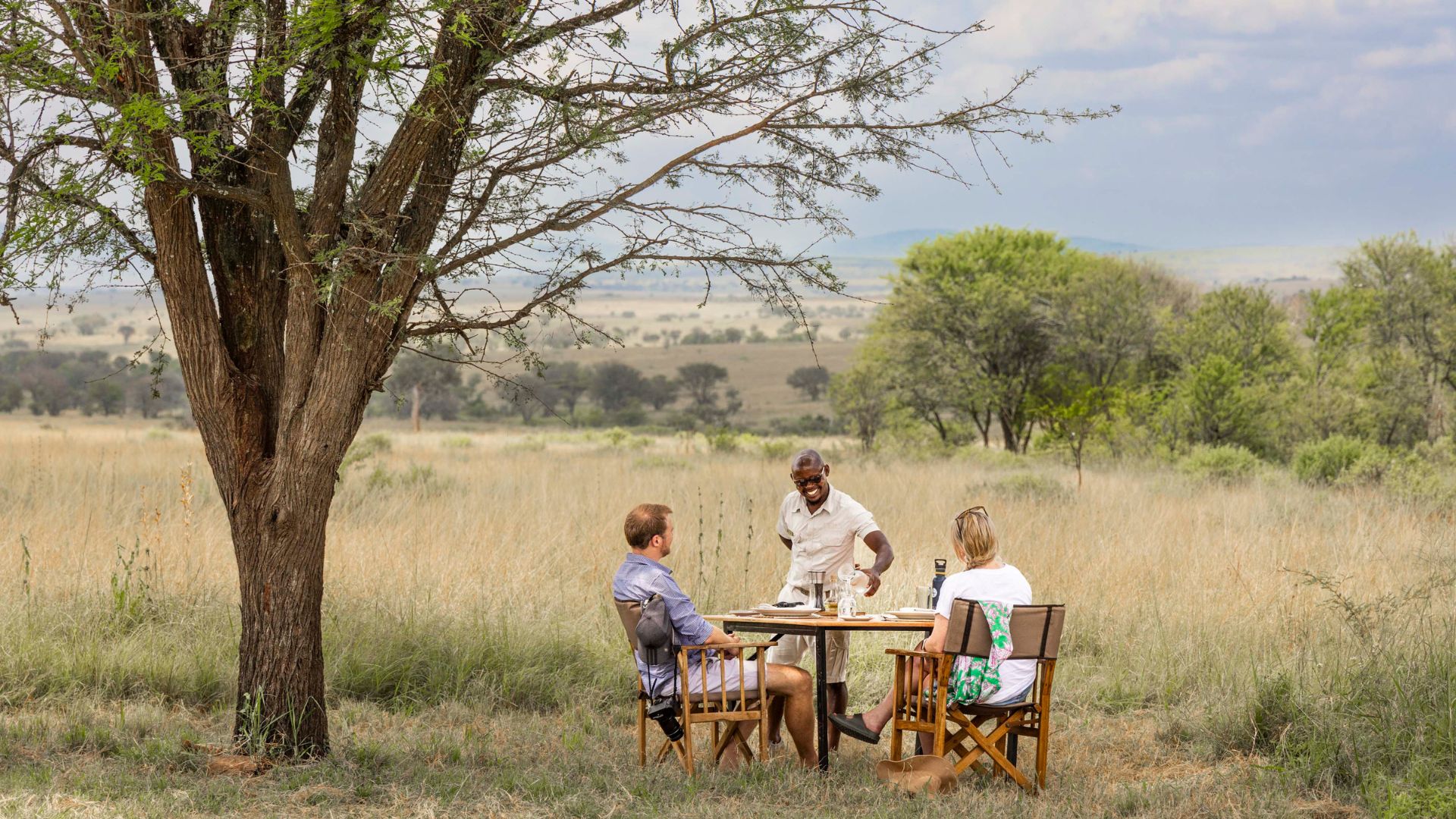 two guests having lunch at olakira migration camp, served by a smiling waiter, tanzania, asilia africa