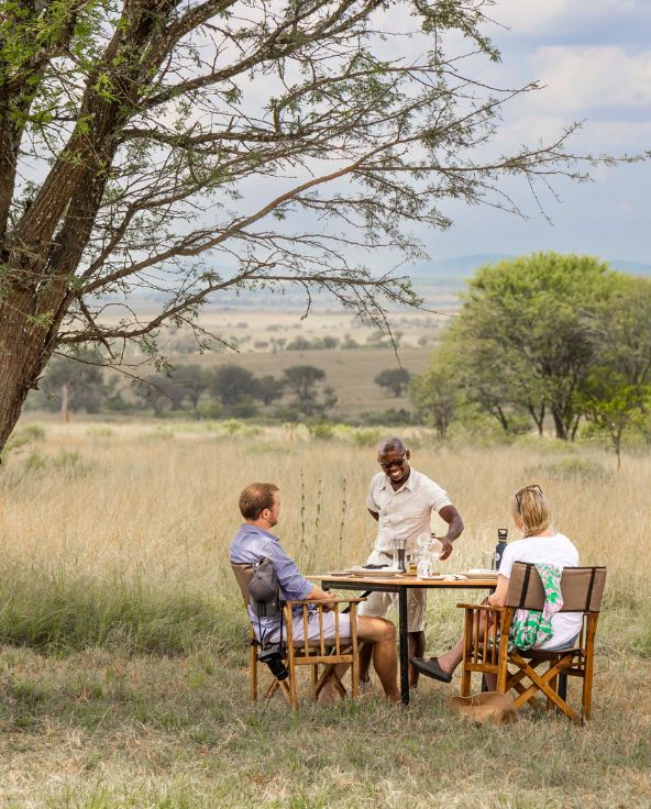 two guests having lunch at olakira migration camp, served by a smiling waiter, tanzania, asilia africa