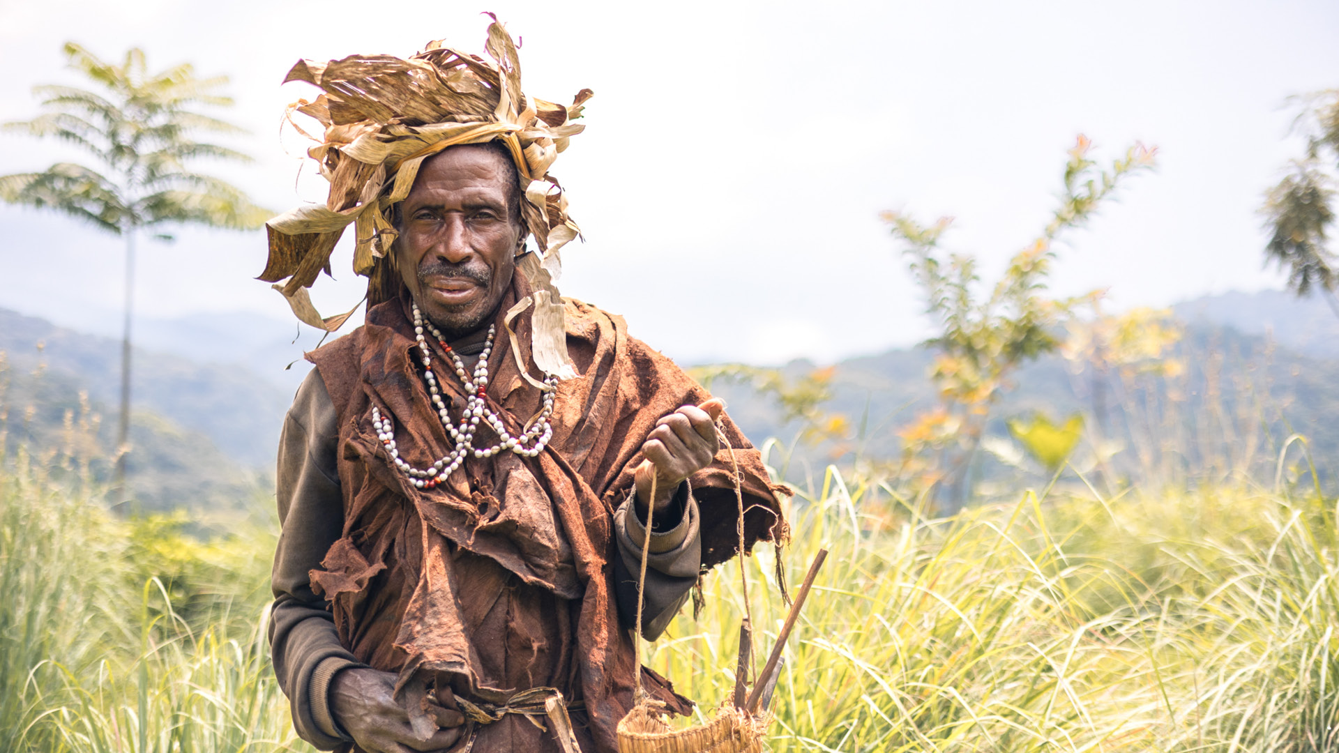 Local tribesman facing the camera with the Bwindi Impenetrable Forest behind him, Erebero Hills, Uganda
