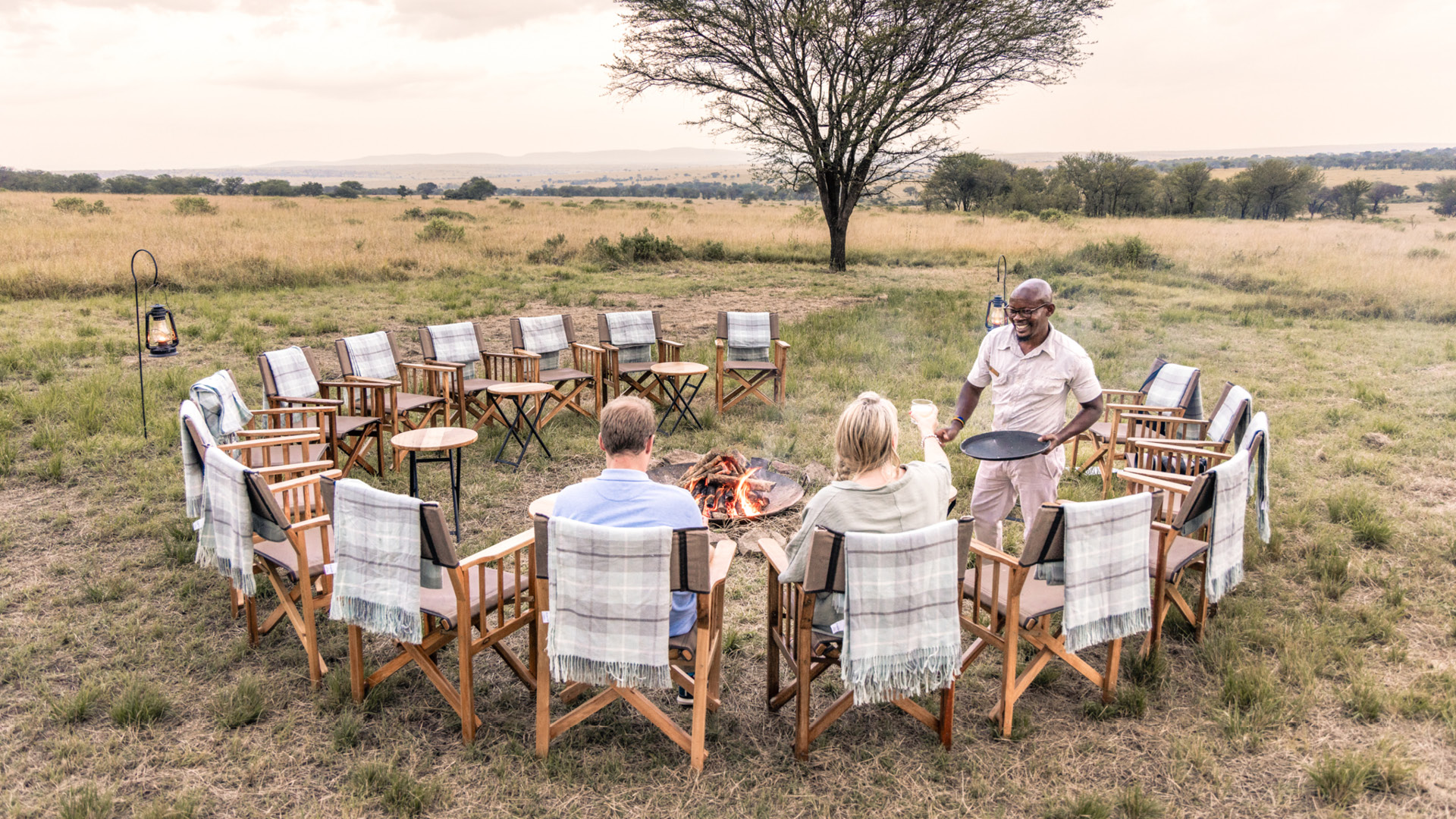 Serengeti National Park, campfire, sundowners, couple with drinks and waiter