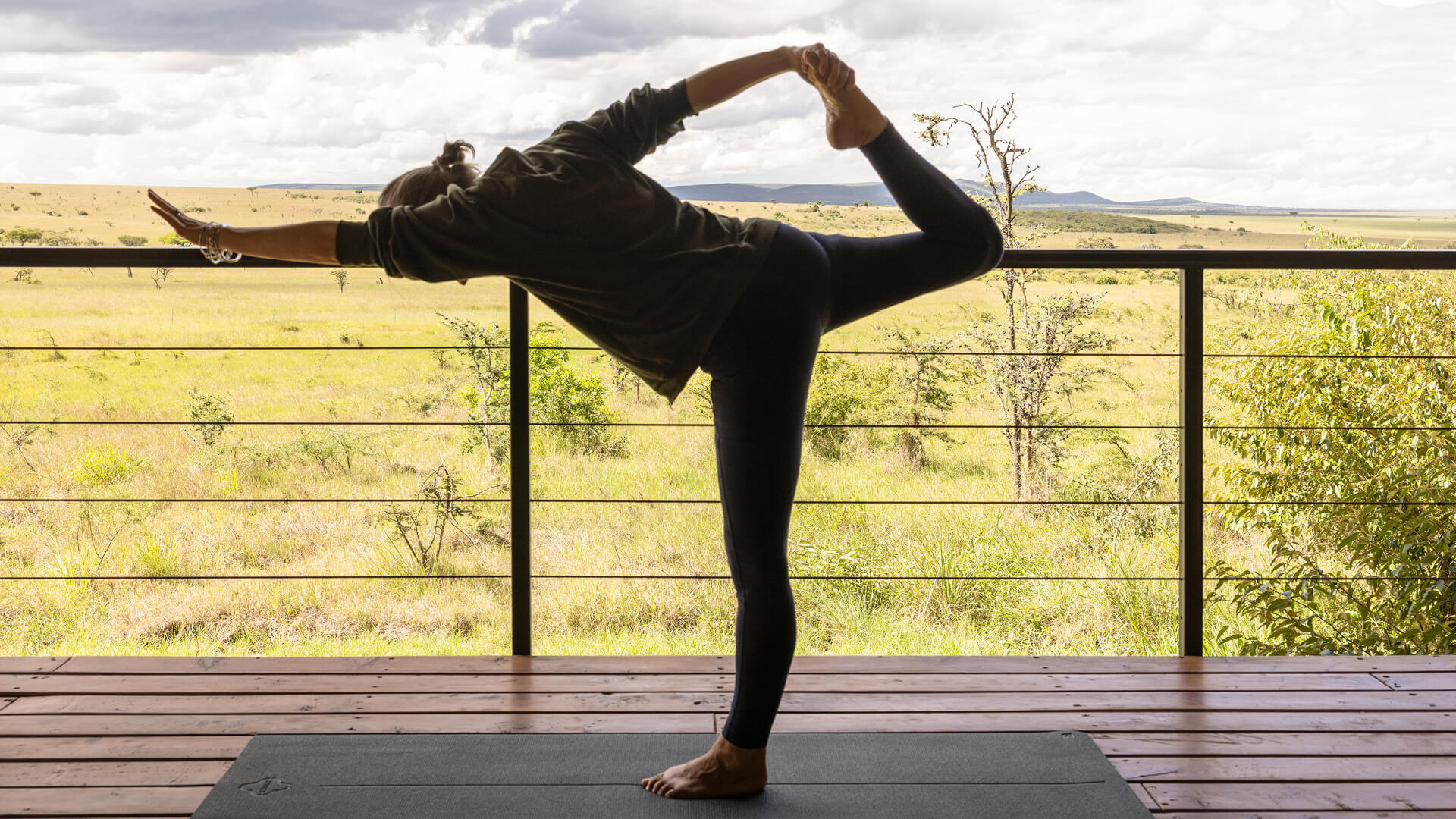 Guest practicing yoga on a wooden deck overlooking the savannah at Naboisho Camp.
