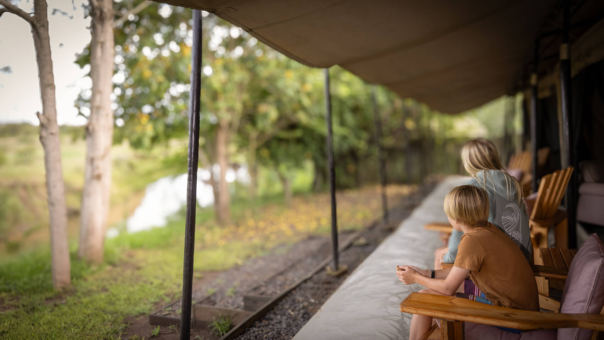Two children unwinding at their tent at Ol Pejeta Bush camp sitting on chairs outside