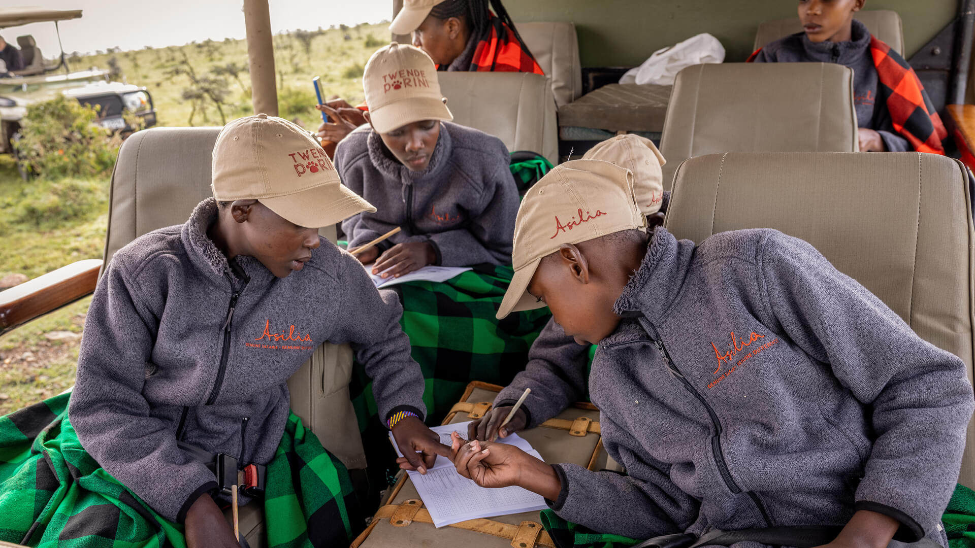 group of Twende students working together to complete a task in the vehicle wearing Asilia jackets and green shukas