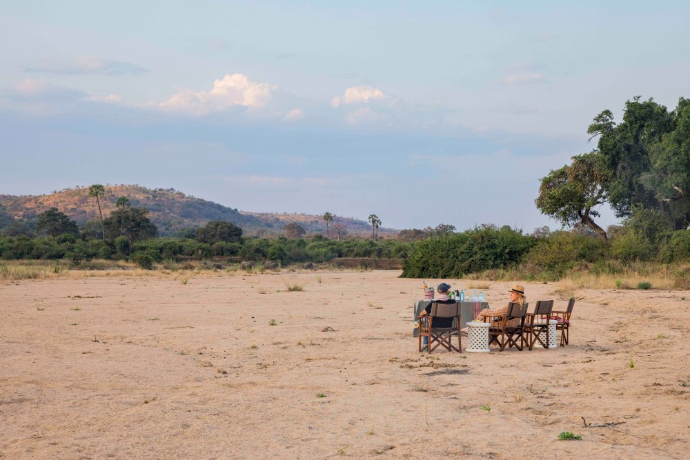 Guests enjoy a sundowner in a dry riverbed in Ruaha National Park, Tanzania.