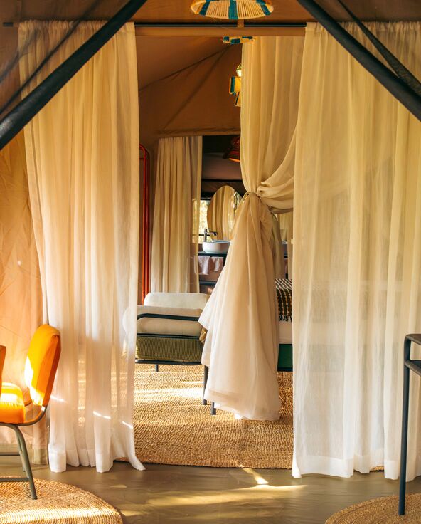 The interior of a luxury safari suite at Emboo with sheer white curtains, woven rugs, soft seating, and warm natural lighting creating a cozy, elegant atmosphere.