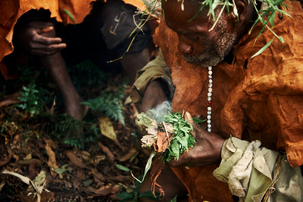 A Batwa elder coaxes a fire to life in Bwindi Forest, Uganda